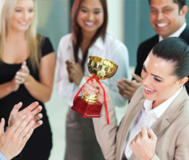 woman holding trophy and team members clapping for her